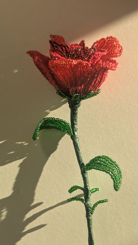 Red beaded flower with green stem and leaves on a beige background