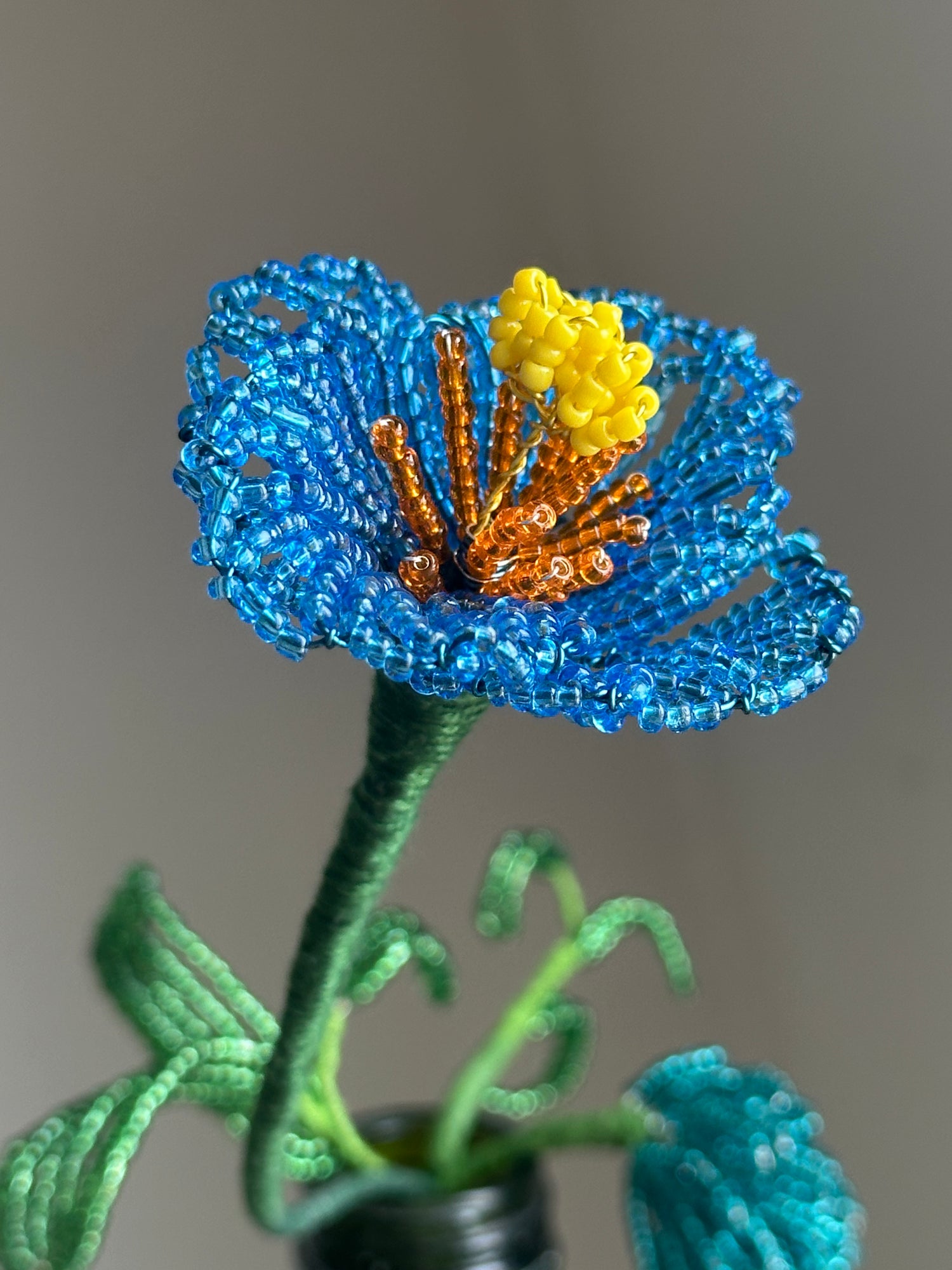 Artificial flower made of blue beads with a yellow center on a gray background