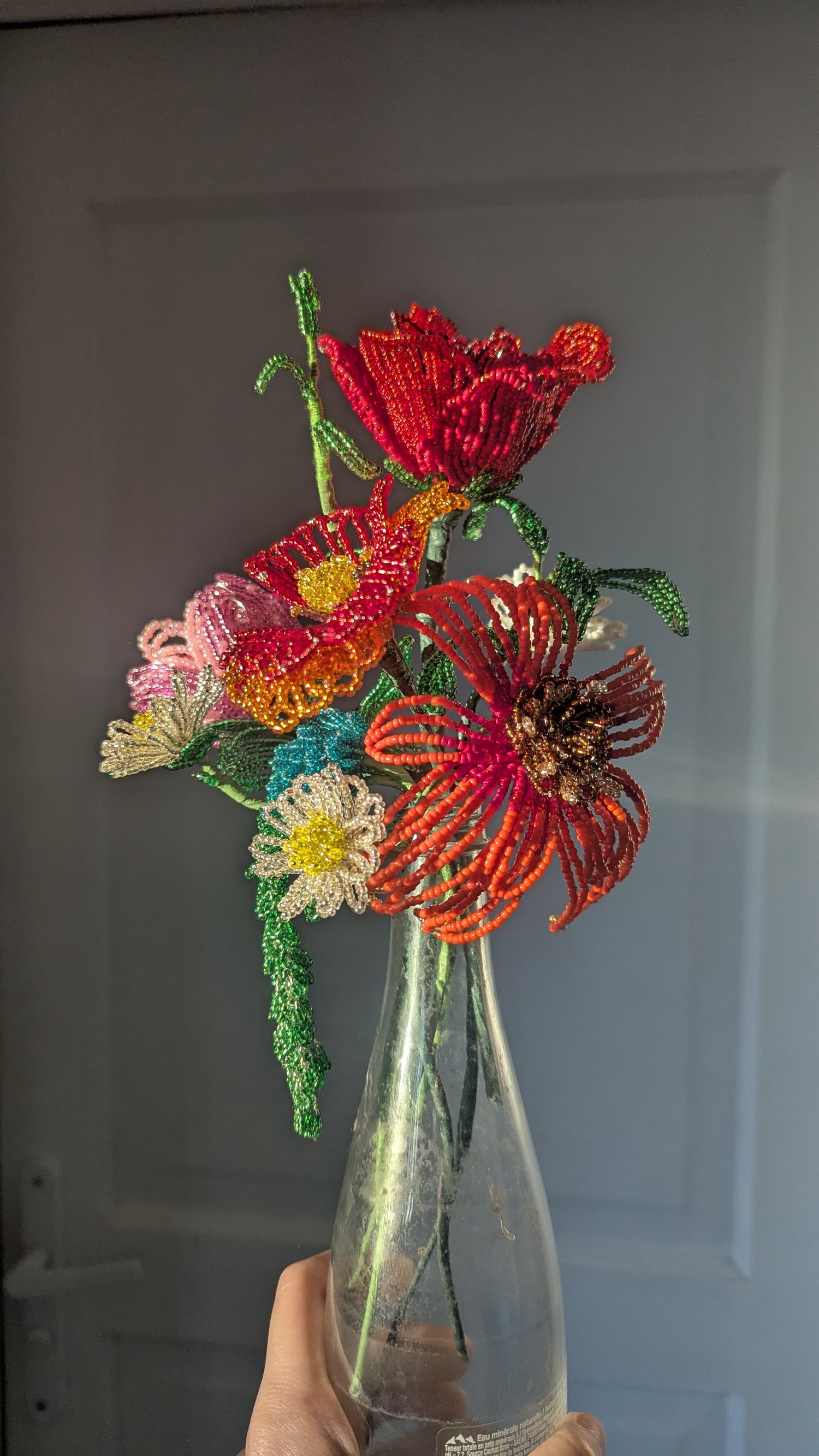 Decorative bouquet of beaded flowers in a clear vase against a neutral background